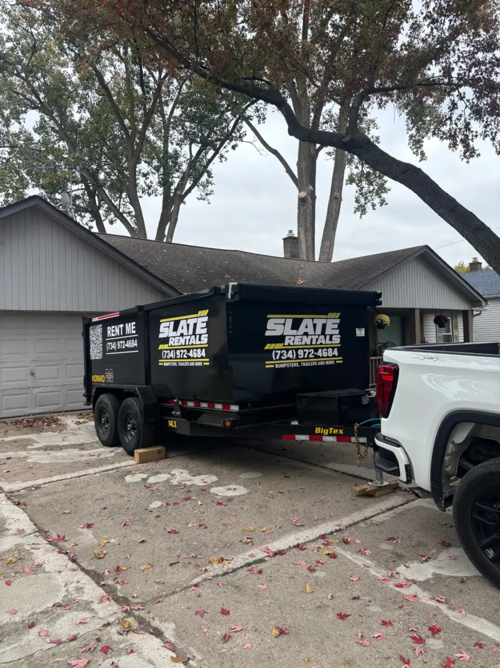 Slate Rentals dump trailer hitched to a white pickup in a driveway, ready to head out.