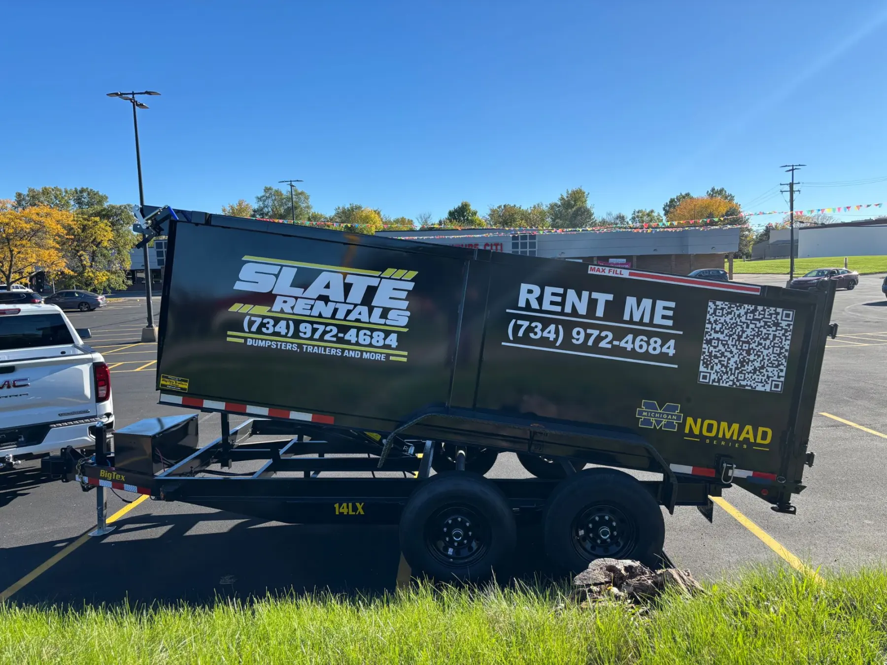 Slate Rentals dump trailer with its bed raised under a clear blue sky.